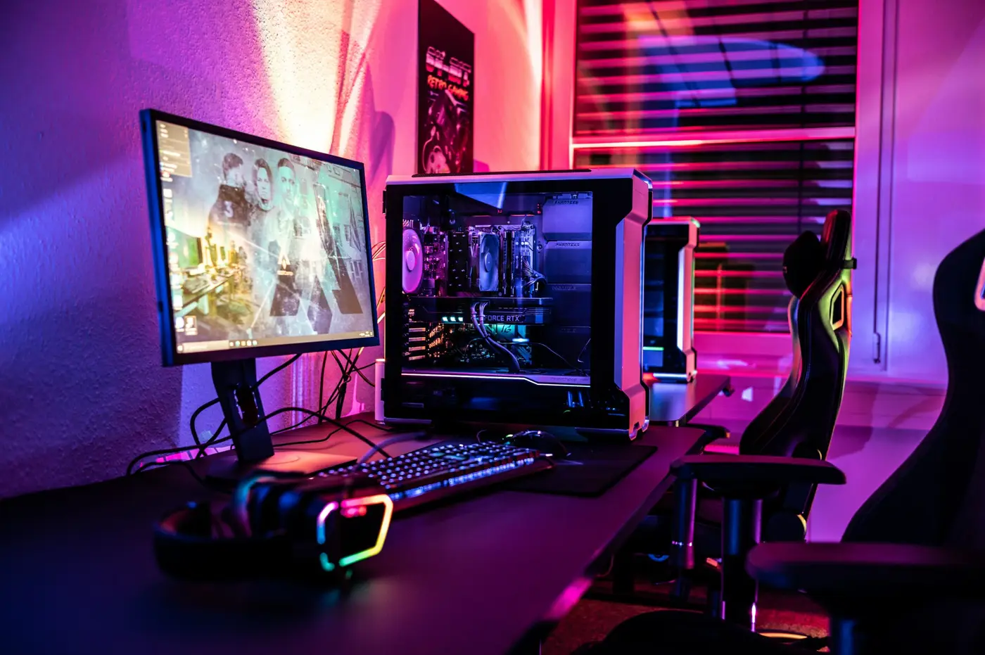 Ein Schreibtisch mit zwei Monitoren, beleuchteter Tastatur und einem Rechner mit farbiger Innenbeleuchtung in Magenta und Türkis.