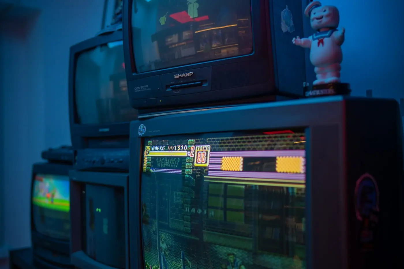 Ein Stapel aus mehreren übereinandergestellten Röhrenfernsehern, auf deren Schirmen verschiedene Spielbilder in blauem Licht laufen.
